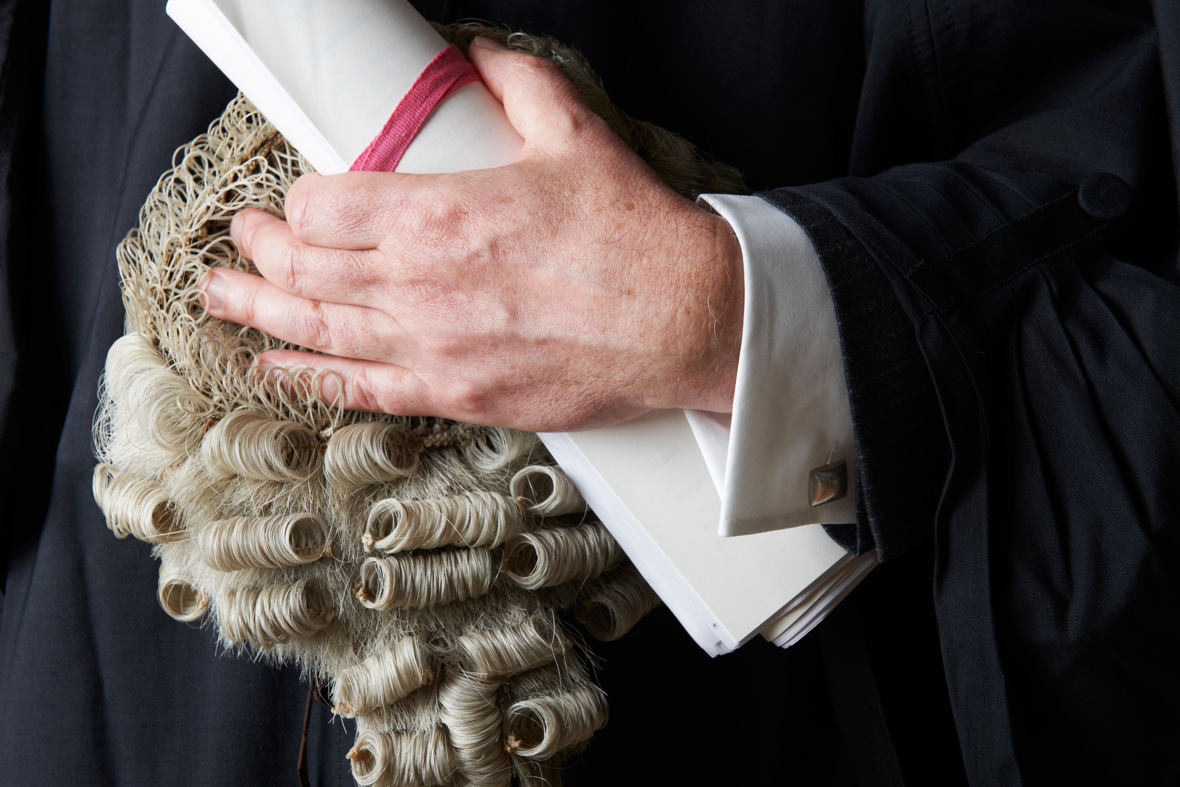 A barrister holding a wig and bundle of documents
